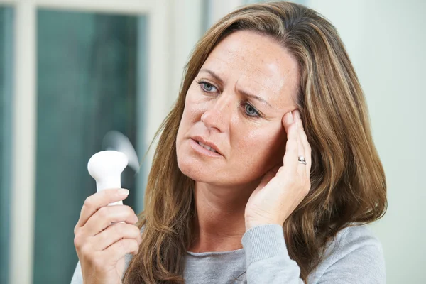 Woman in Perimenopause having a Hot Flash and Holding a Fan in Front of her Face
