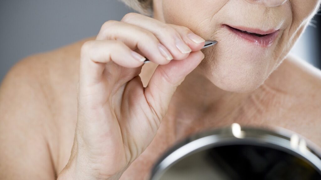 Brave woman plucking her midlife chin hair like a true menopausal warrior.