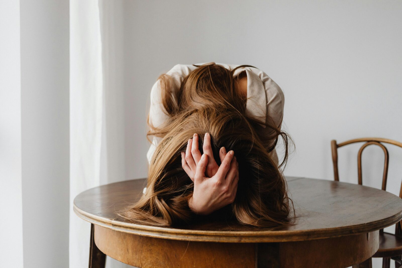 Stressed middle-aged woman with head in hands on table — visual metaphor for perimenopause anxiety and hormonal overwhelm.